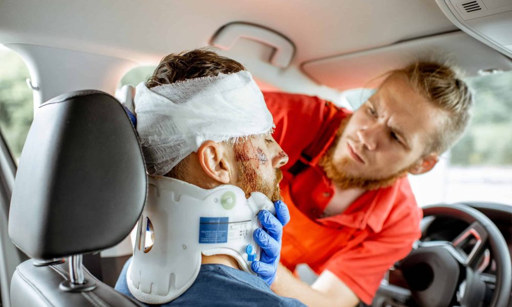 Medic providing emergency medical assistance after the road accident Medic applying bandage on the head of victim with serious damages sitting on the driver seat after the road accident. Providing emergency medical assistance